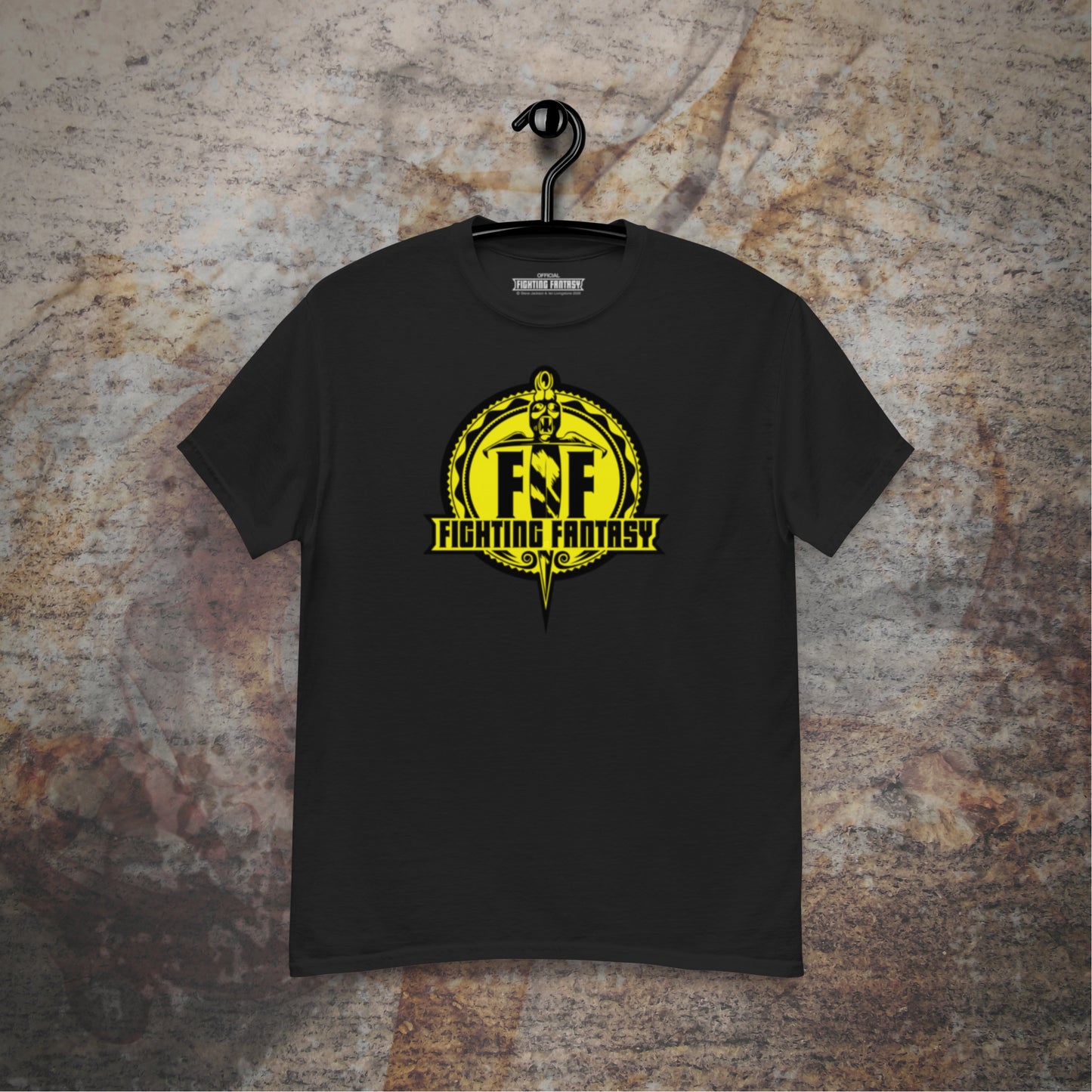 Fighting Fantasy logo design on a black t-shirt hanging in front of a stone wall background.
