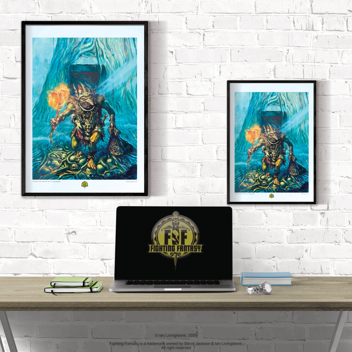 Two framed art prints featuring a stylized blue and gold fantasy creature are displayed on a white brick wall above a desk with a laptop, glasses, and books. The laptop screen shows the Fighting Fantasy logo.